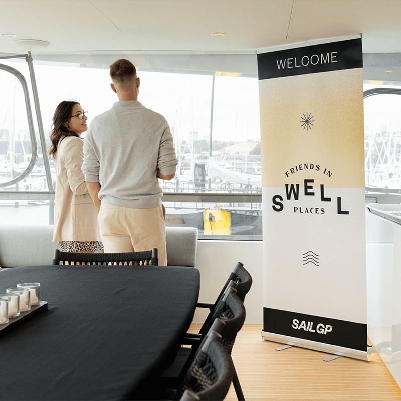 People standing on boat with a Sail GP Friends in Swell Places branded flag stand